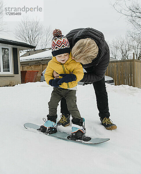 Liebevoller Vater umarmt seinen Sohn  der im Winter Snowboarden lernt