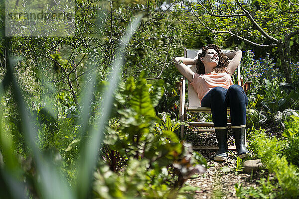 Junge Frau entspannt sich auf einem Stuhl im Garten an einem sonnigen Tag