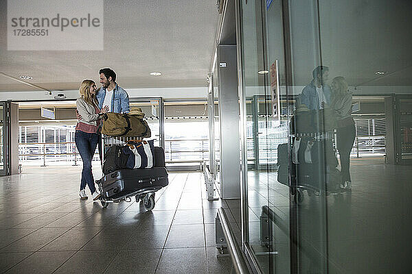 Glückliches junges Paar mit Gepäckwagen im Flughafenterminal