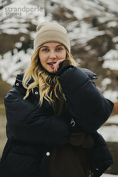 Blonde Frau mit Strickmütze vor einem Schneeberg
