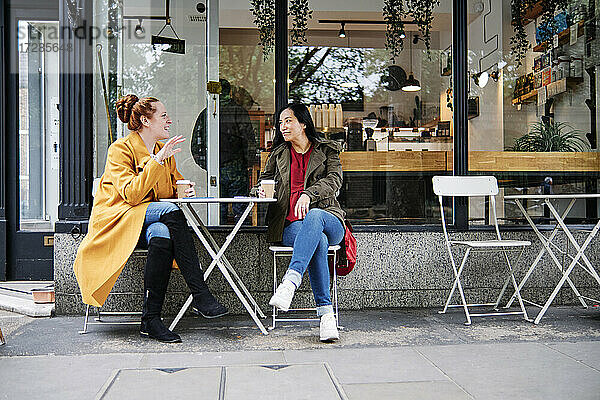 Frau gestikuliert im Gespräch mit einer Freundin vor einem Café