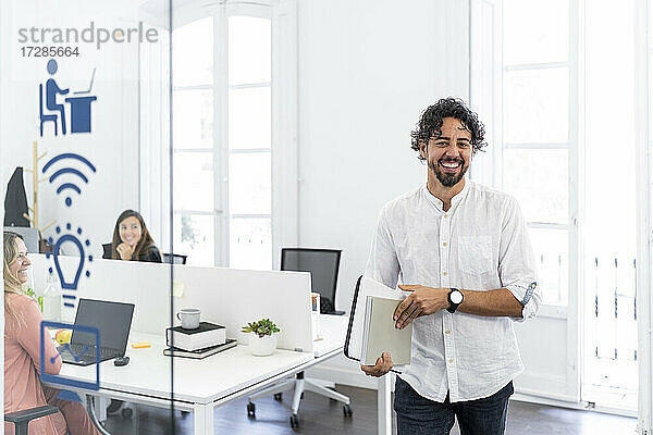 Lächelnder männlicher Unternehmer  der nach einer Besprechung aus einer Bürozelle geht