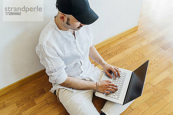 Junger Mann benutzt Laptop  während er zu Hause auf dem Boden sitzt