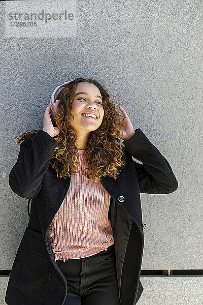 Junge Frau hört Musik über Kopfhörer vor einer Wand