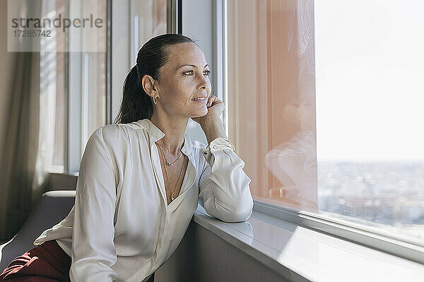 Schöne Unternehmerin schaut durch das Fenster  während sie im Büro sitzt