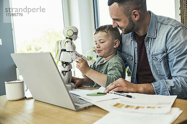 Lächelnder Mann schaut auf seinen Sohn  der zu Hause mit einem Roboter spielt