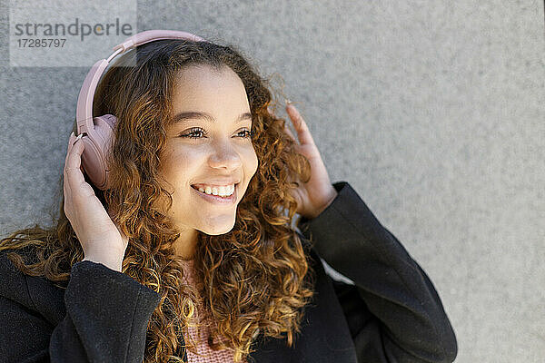 Lächelnde junge Frau hört Musik über Kopfhörer