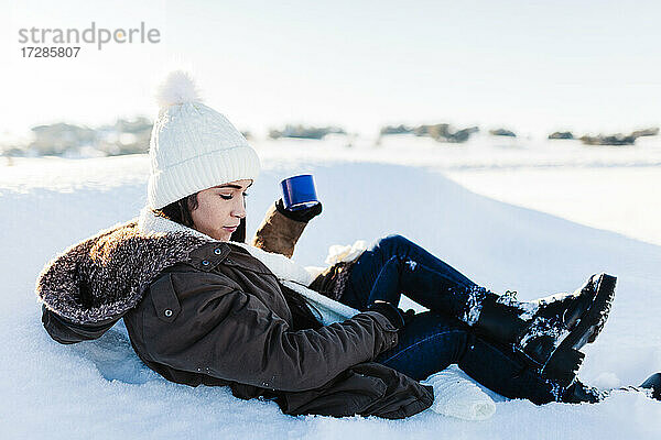 Frau hält Kaffeetasse und entspannt sich im Schnee im Urlaub