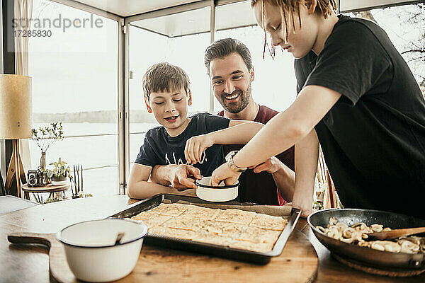 Lächelnder Vater mit Söhnen bei der Essenszubereitung in der Küche eines Hausbootes