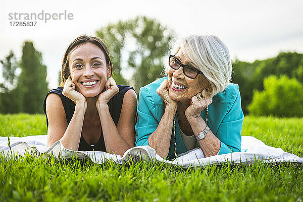 Lächelnde Frauen mit Händen am Kinn auf einer Picknickdecke liegend