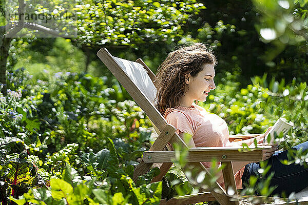 Frau liest ein Buch und sitzt auf einem Stuhl im Garten
