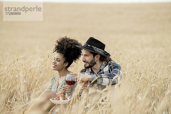 Lächelndes erwachsenes Paar  das auf einem Feld sitzt und wegschaut