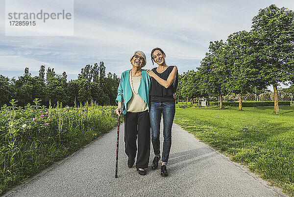 Lächelnde Großmutter und Enkelin gehen zusammen auf der Straße im Park