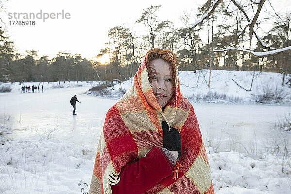 Lächelnde Frau  die sich im Winter mit einer Decke zudeckt