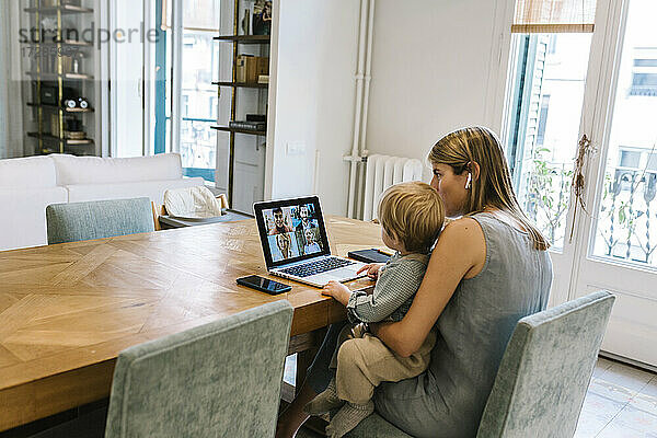 Junge sitzt mit seiner Mutter während einer Videokonferenz über einen Laptop zu Hause