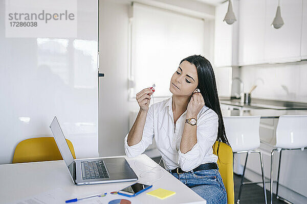 Frau trägt In-Ear-Kopfhörer  während sie im Büro zu Hause sitzt