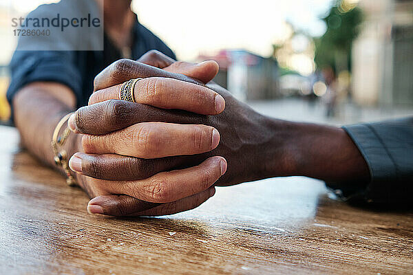 Multiethnisches schwules Paar hält sich am Tisch eines Straßencafés an den Händen