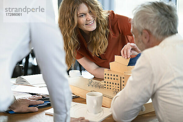 Architektin  die ein Modell arrangiert  während sie mit männlichen Kollegen im Büro diskutiert