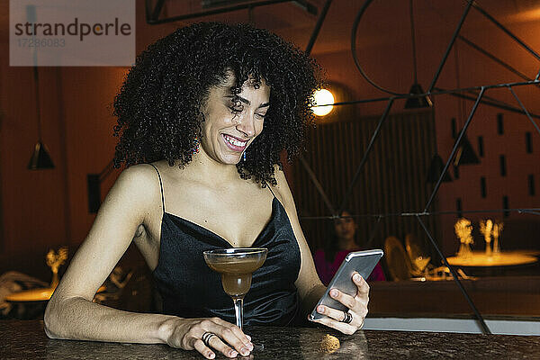 Lächelnde Frau  die ein Mobiltelefon bei einem Getränk auf dem Tisch benutzt