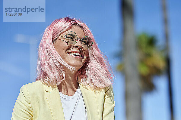 Fröhliche junge Frau mit rosa Haaren  die an einem sonnigen Tag wegschaut