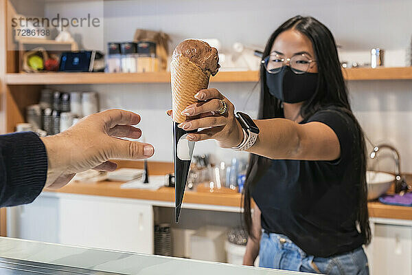 Eine Mitarbeiterin gibt einem Kunden in einem Geschäft während COVID-19 ein Eis.