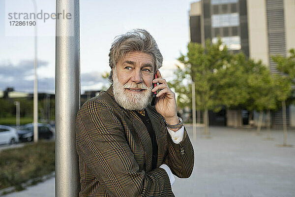 Älterer Geschäftsmann lehnt sich an einen Pfahl  während er mit seinem Handy in der Stadt telefoniert
