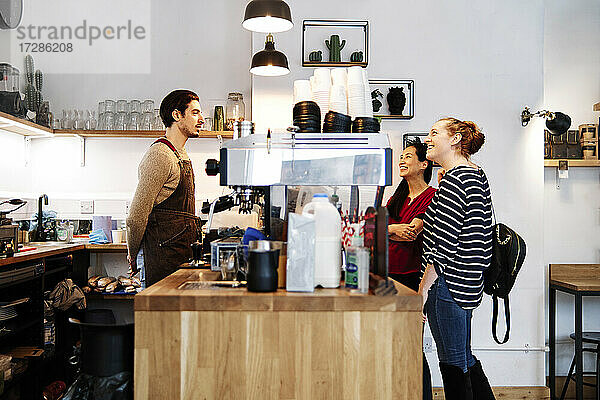 Lächelnde weibliche Kunden  die eine Hängelampe betrachten  während sie vor dem Besitzer eines Cafés stehen