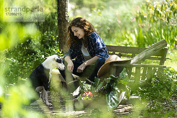 Frau sitzt auf Holzbank mit Hund im Garten