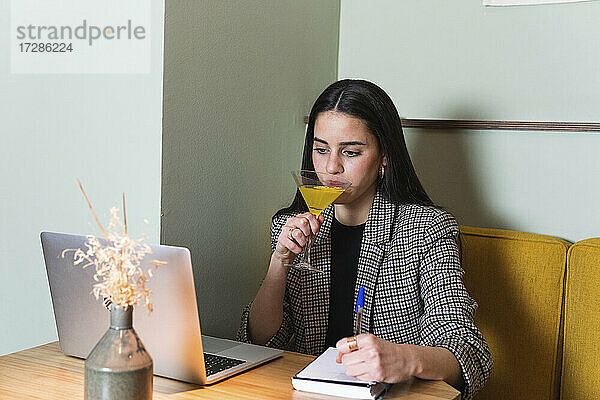 Geschäftsfrau trinkt etwas  während sie im Restaurant am Laptop arbeitet