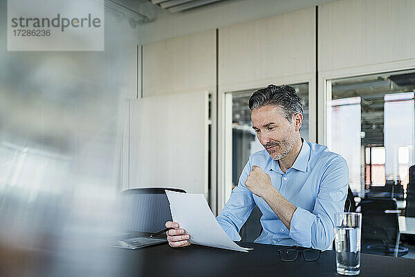 Männlicher Berufstätiger  der Dokumente liest  während er am Schreibtisch im Büro sitzt
