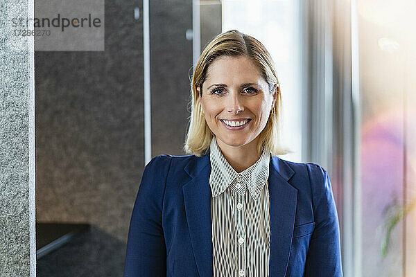 Lächelnde Geschäftsfrau mit blondem Haar im Büro stehend