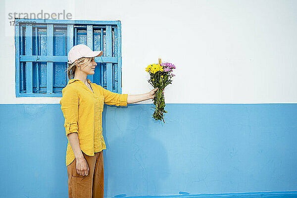 Junge Frau mit Mütze hält Blumen an der Wand