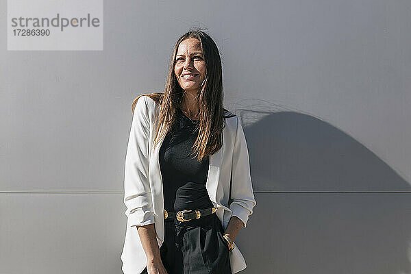 Lächelnde reife Geschäftsfrau steht vor einer grauen Wand
