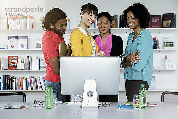 Lächelnde männliche und weibliche Unternehmer arbeiten vor einem Computer im Büro