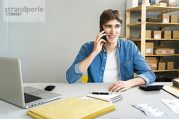 Lächelnder Geschäftsmann  der im Büro sitzt und mit seinem Handy telefoniert
