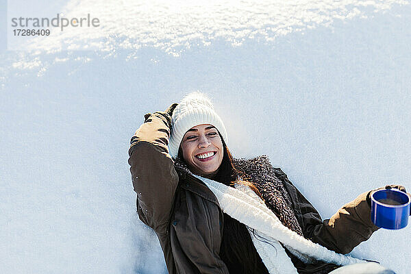 Fröhliche Frau genießt Kaffee im Schnee