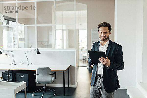 Männlicher Unternehmer mit digitalem Tablet  der lächelnd im Büro steht