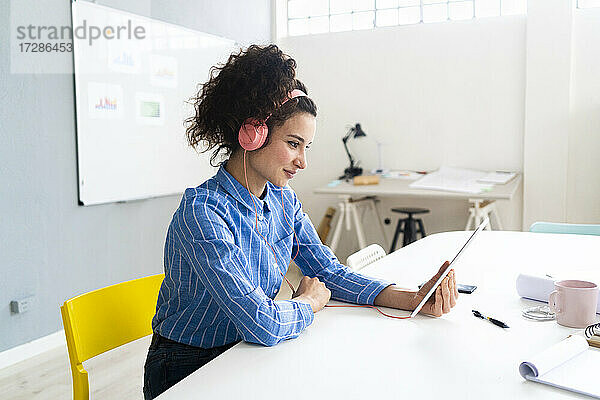 Unternehmerin mit Kopfhörern und digitalem Tablet bei der Arbeit im Kreativbüro