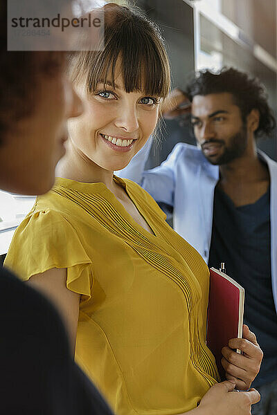 Lächelnde schöne junge Frau mit männlichen und weiblichen Kollegen im Büro stehend