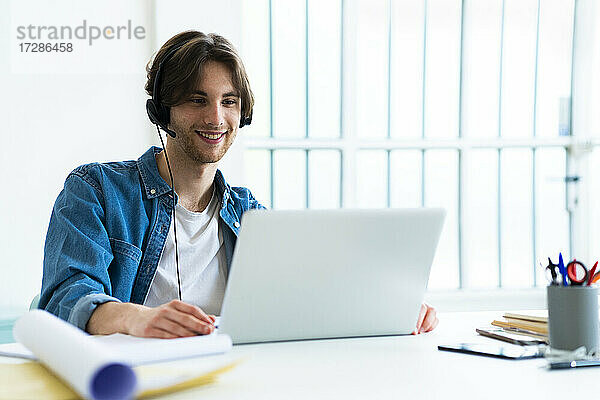 Lächelnder Geschäftsmann mit Headset und Laptop bei der Arbeit im Büro