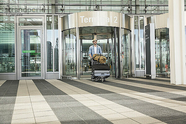 Junger Mann mit Gepäckwagen im Flughafenterminal