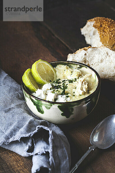 Schüssel mit griechischer Avgolemono-Suppe mit Reis  Zitronenscheiben und Brot