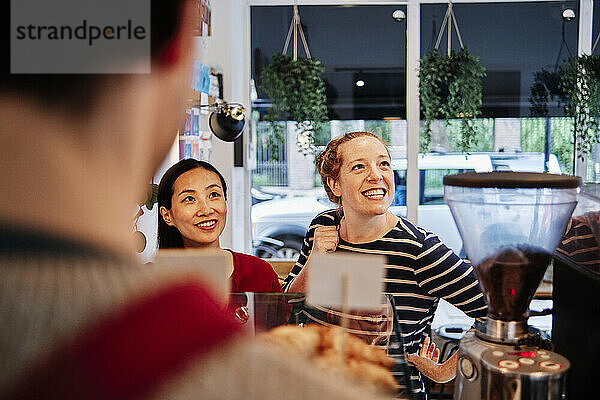 Lächelnde Freundinnen schauen weg  während sie vor dem Besitzer eines Cafés stehen