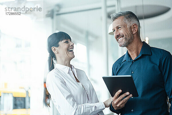 Lächelnder Geschäftsmann mit digitalem Tablet  der neben einem Kollegen im Cafe steht