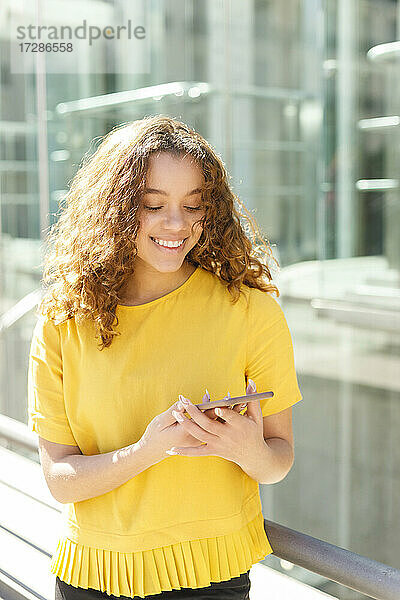 Lächelnde junge Frau  die an einem sonnigen Tag ein Mobiltelefon benutzt