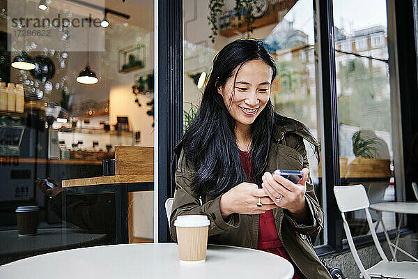 Lächelnde schöne Frau  die ein Mobiltelefon in einem Straßencafé benutzt