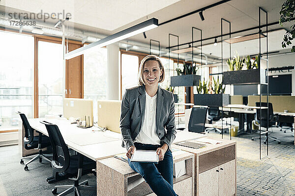 Lächelnde Geschäftsfrau mit digitalem Tablet auf dem Schreibtisch im Büro