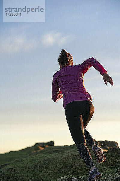 Junge Frau läuft bei Sonnenaufgang auf einen Hügel