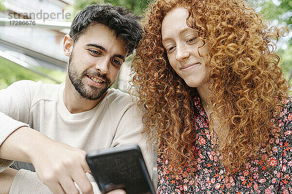 Junger Mann mit Freundin bei der Nutzung eines Smartphones
