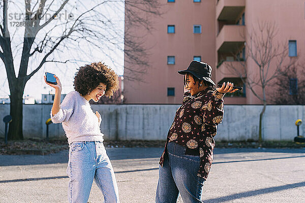 Fröhliche Freunde mit Mobiltelefon tanzen auf der Straße
